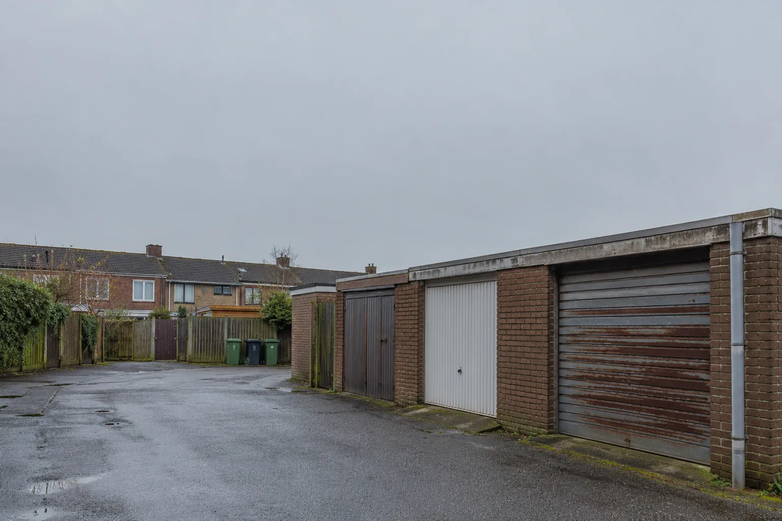 Een rij garages van baksteen met roldeuren in een stille achterstraat, met rijtjeshuizen in de verte.